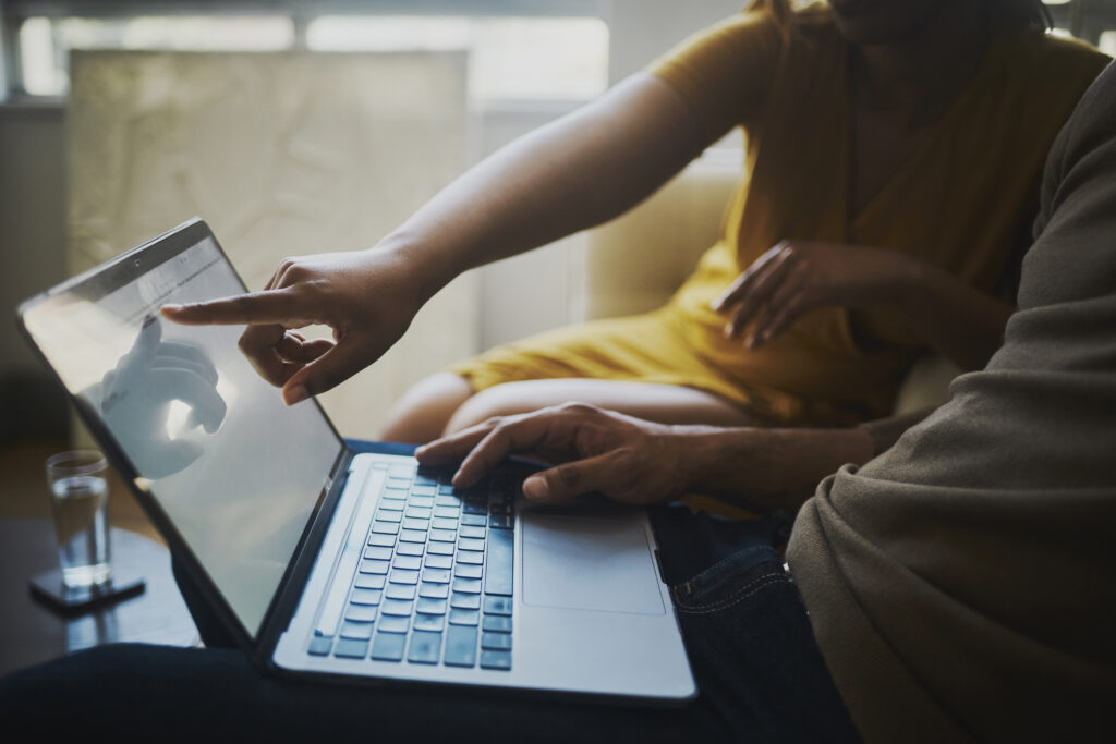 A close-up image of the hands of a business man and woman diligently discussing and working on a laptop computer.